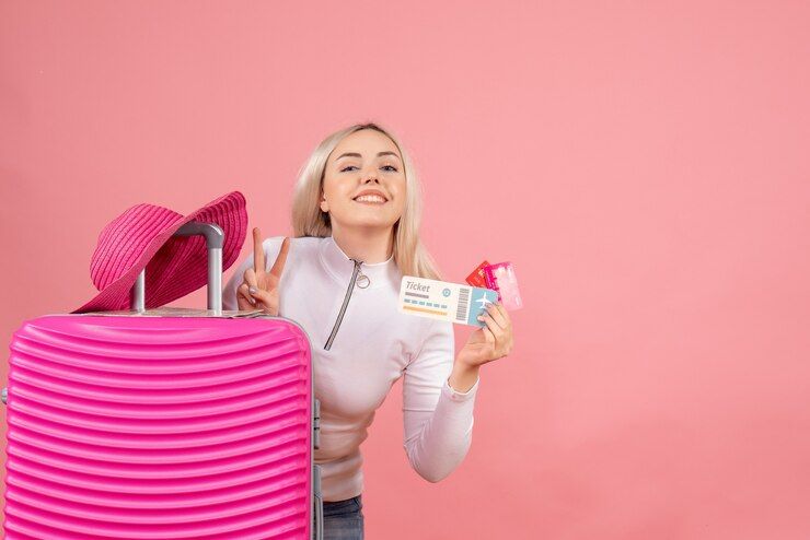 front-view-blonde-woman-with-pink-suitcase-holding-ticket-and-card-making-victory-sign_179666-33804.jpg